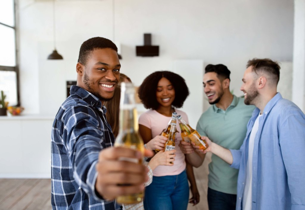 Group of young flatmates drinking beer in their house, saying cheers and celebrating