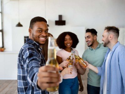 Group of young flatmates drinking beer in their house, saying cheers and celebrating