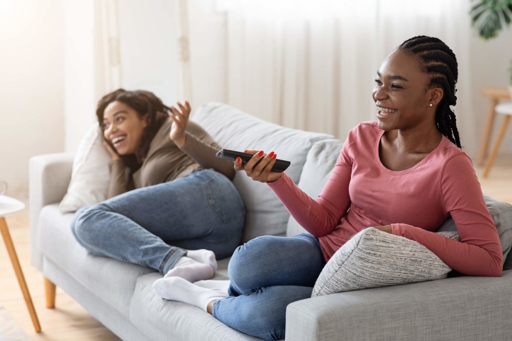 Two housemates hanging out, watching TV and laughing