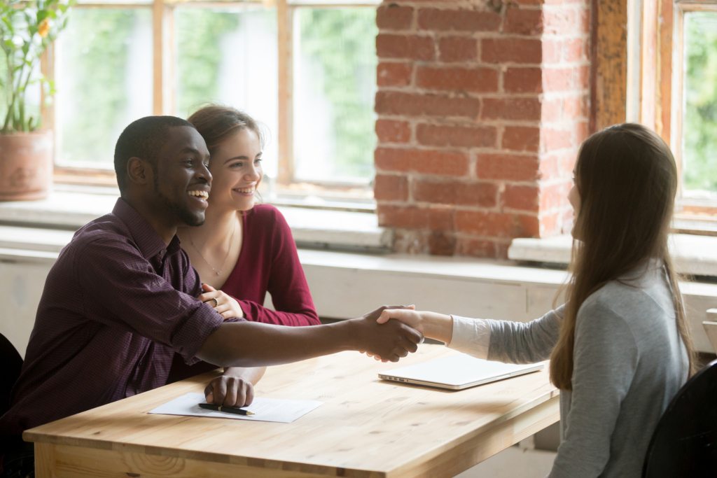 Happy smiling man shaking hands with real estate agent. Husband and wife signed rental lease agreement.