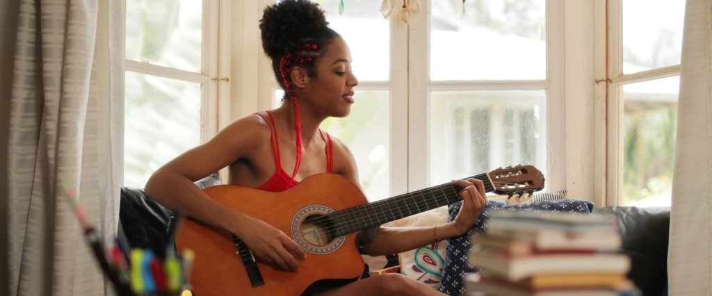 Girl lying on couch and singing with guitar in Leeds home.