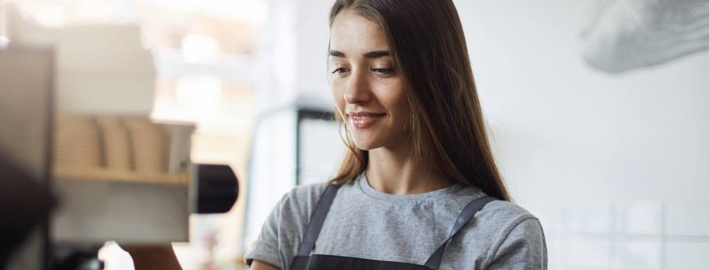 Female student on her summer job serving coffee working as a barista in a local pastry shop