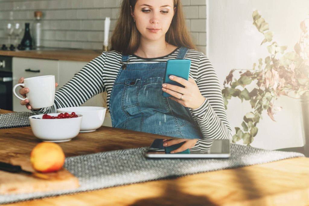 a pregnant student sat the table studying and using phone