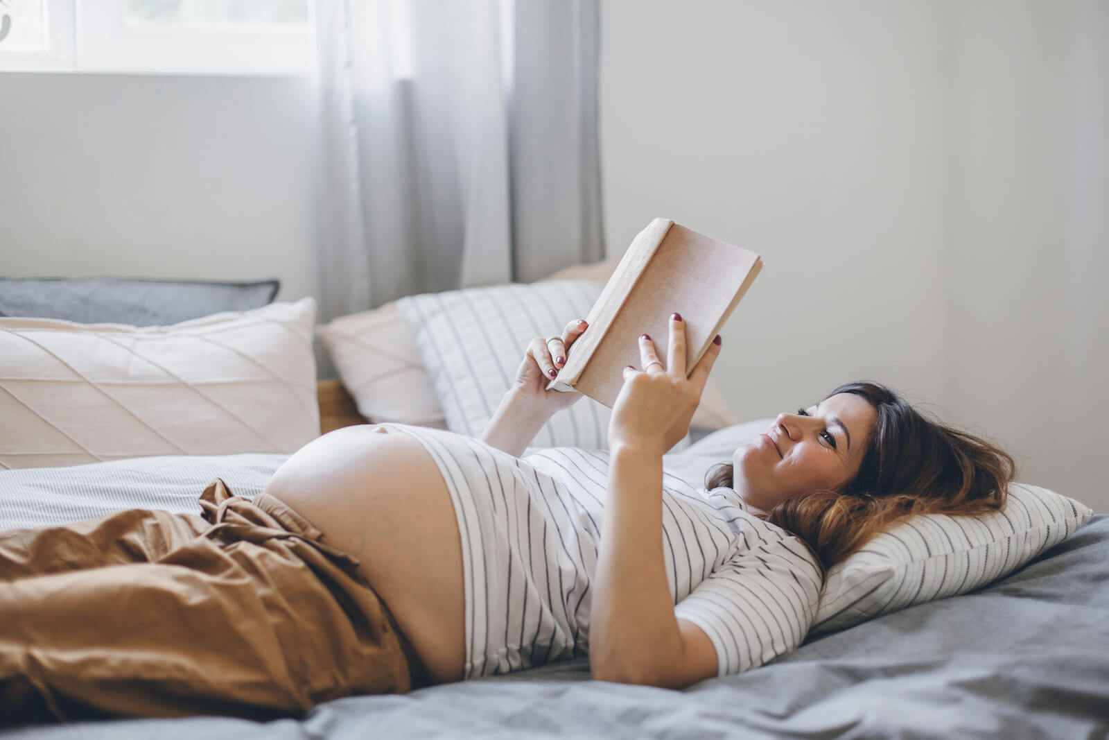 a pregnant student reading in bed