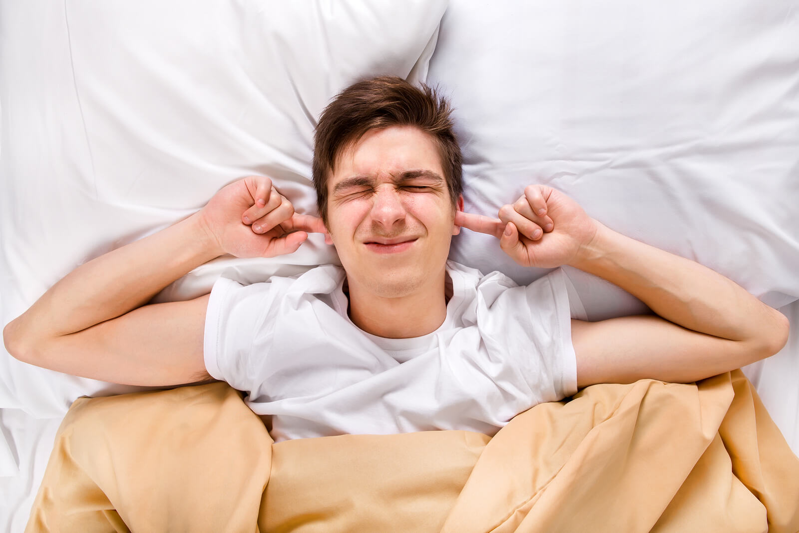 a man in bed covering his ears to block noise from noisy housemates in house share