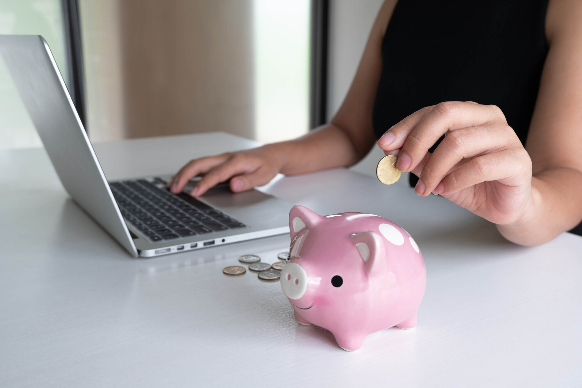 a woman using her laptop and saving in her piggy bank