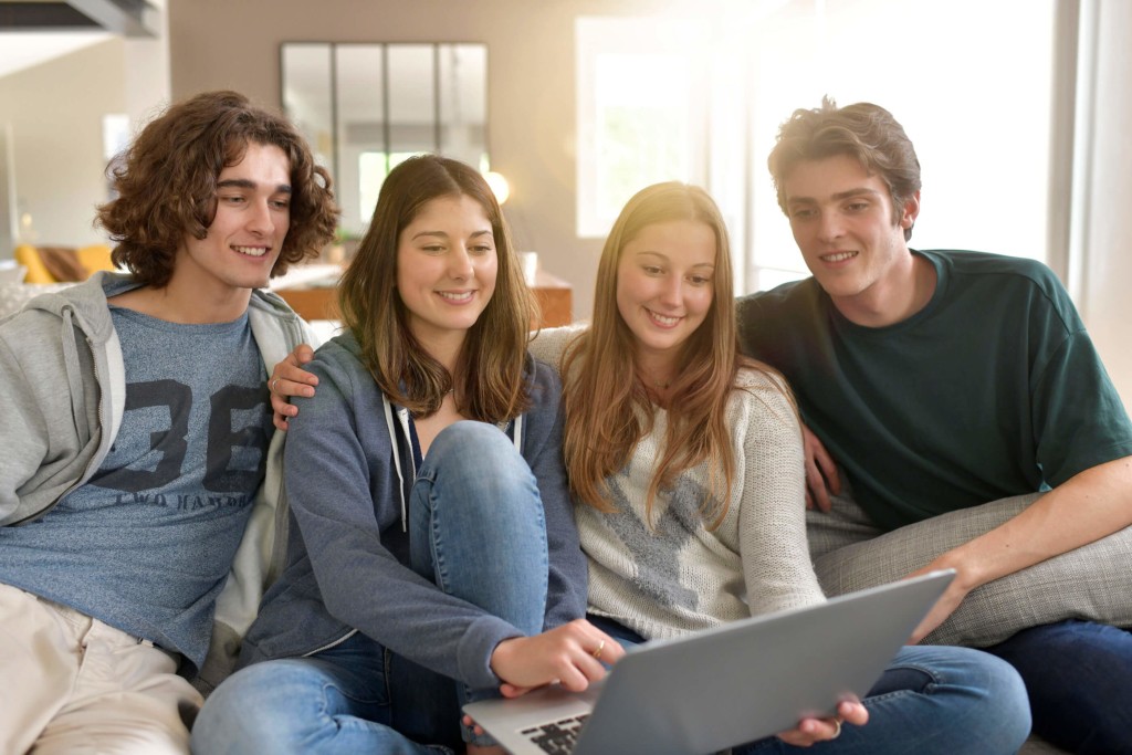 Group of four flatmates hanging out, looking at a laptop