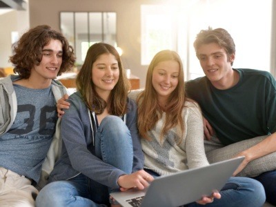 Group of four flatmates hanging out, looking at a laptop
