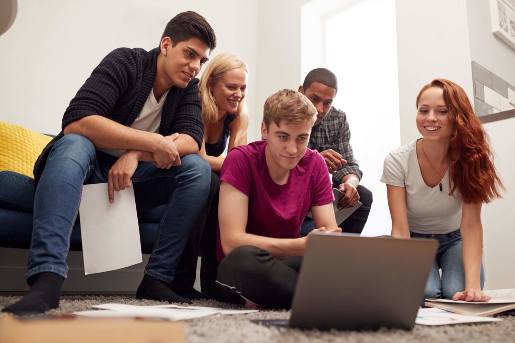 A group of university students, sat around a laptop, watching the screen