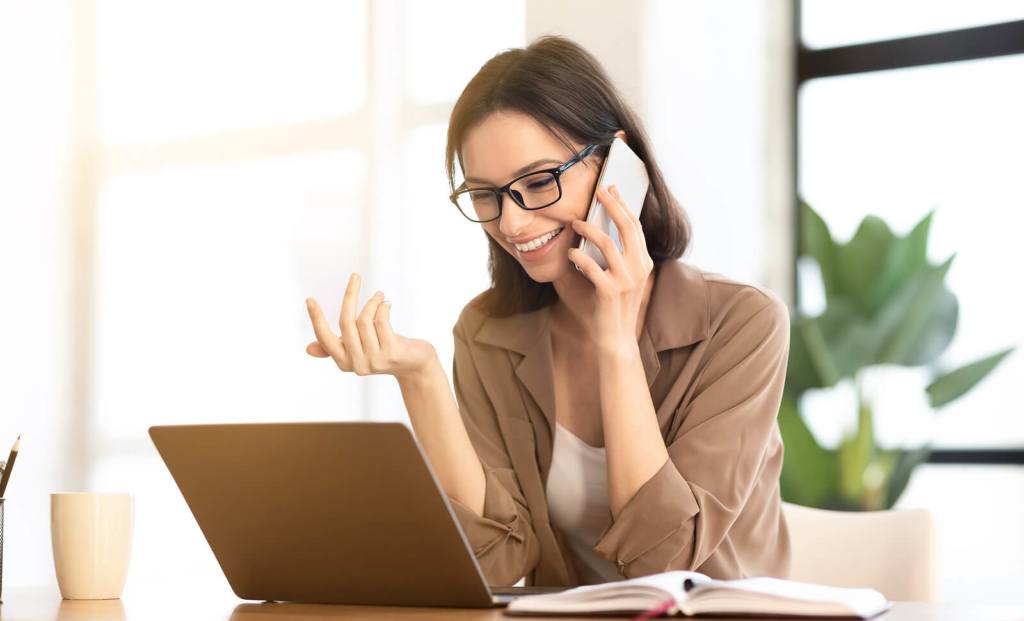A happy young professional woman on the phone while using her laptop