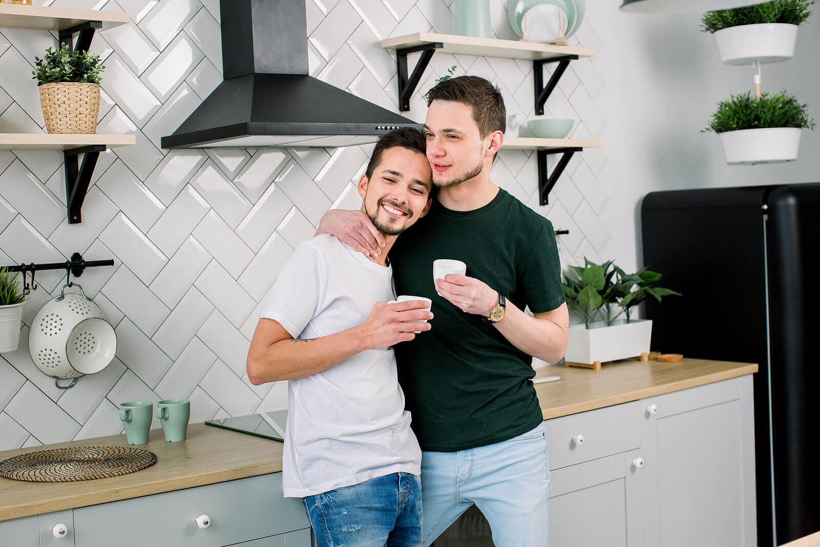 A male gay couple hugging and drinking coffee in a house share