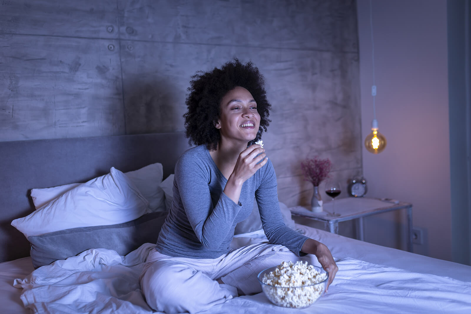 A woman eating popcorn and watching TV in her bedroom, alone