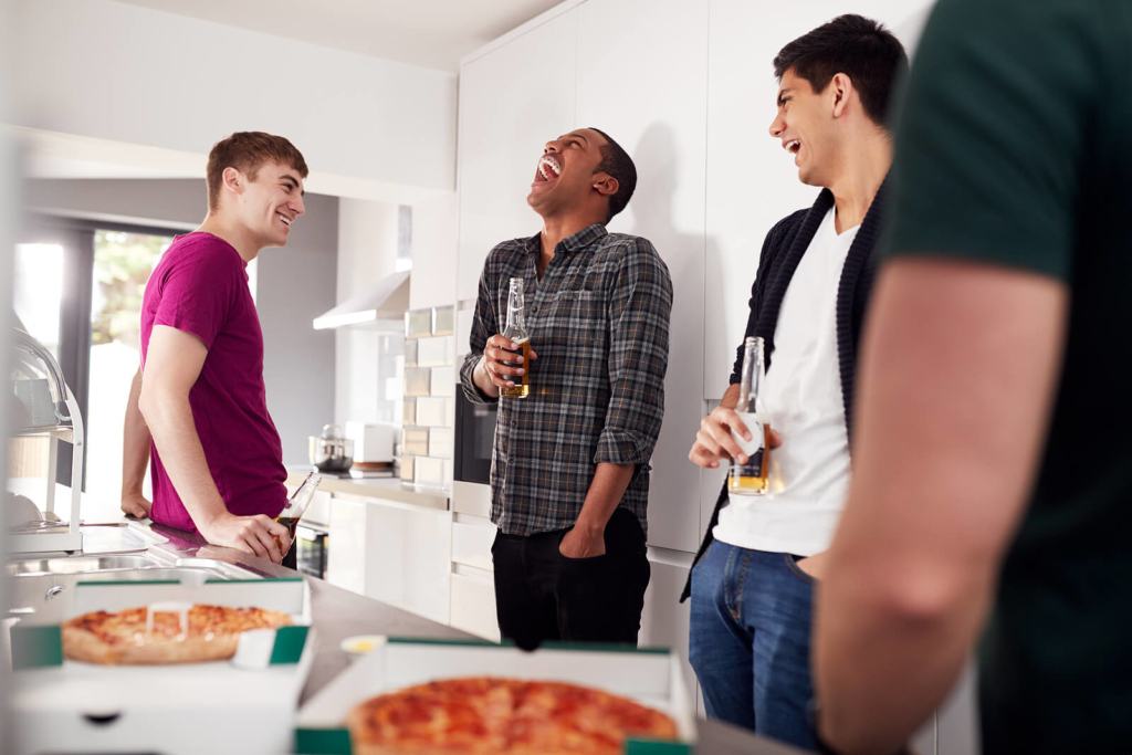 men laughing in the kitchen with drinks and beers.