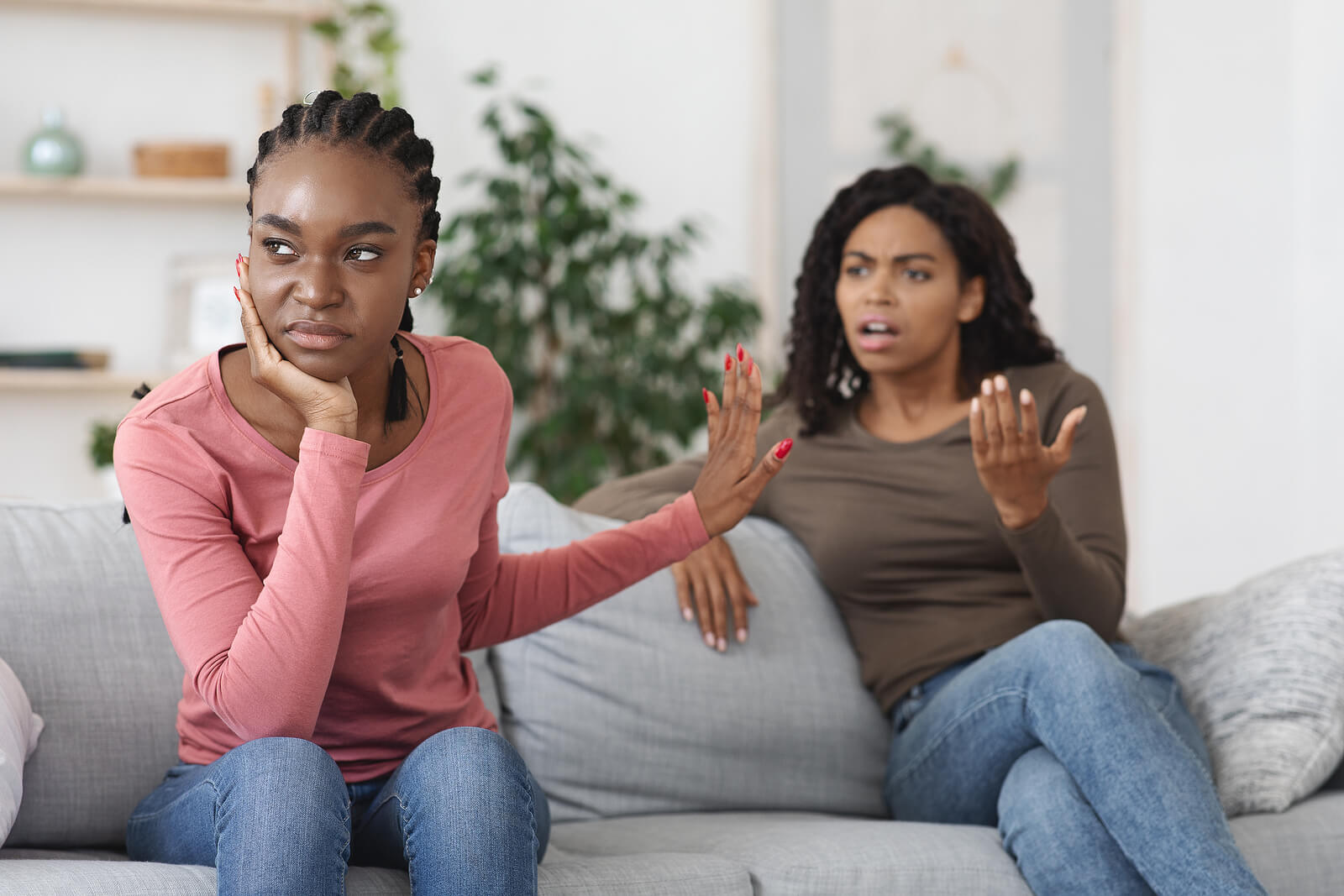 Two annoyed black woman sat on a sofa, falling out with each other in their house share