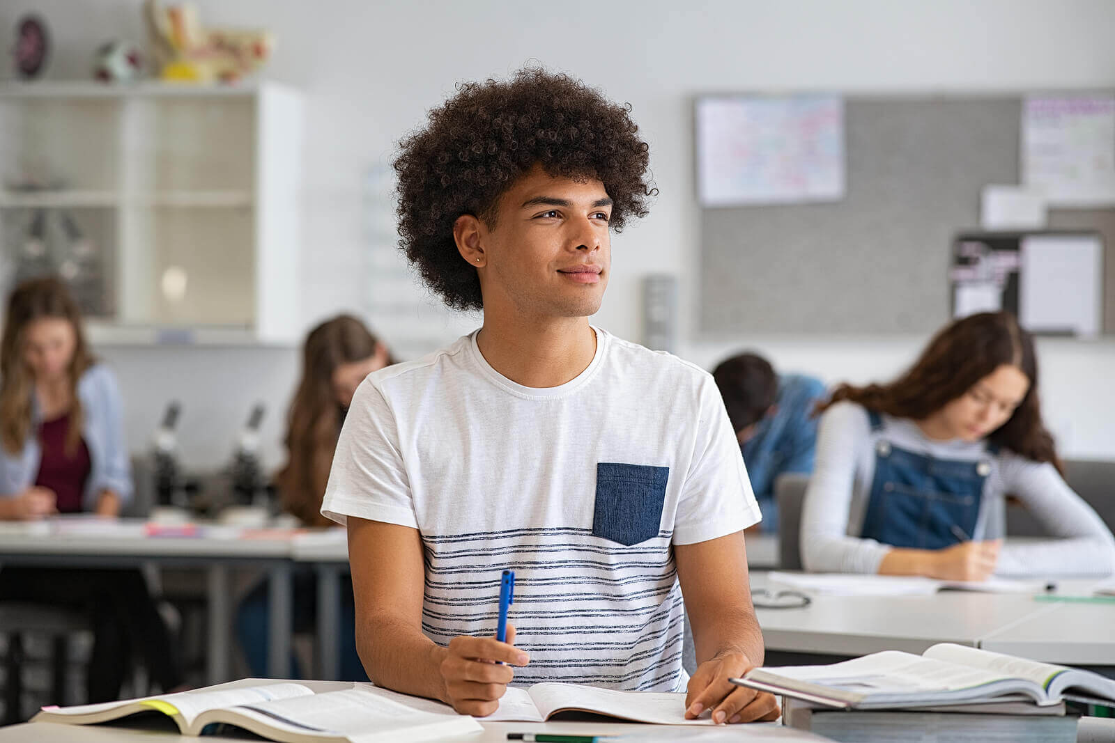 A young Black male student sitting an exam at university, smiling as he gazes out of the window