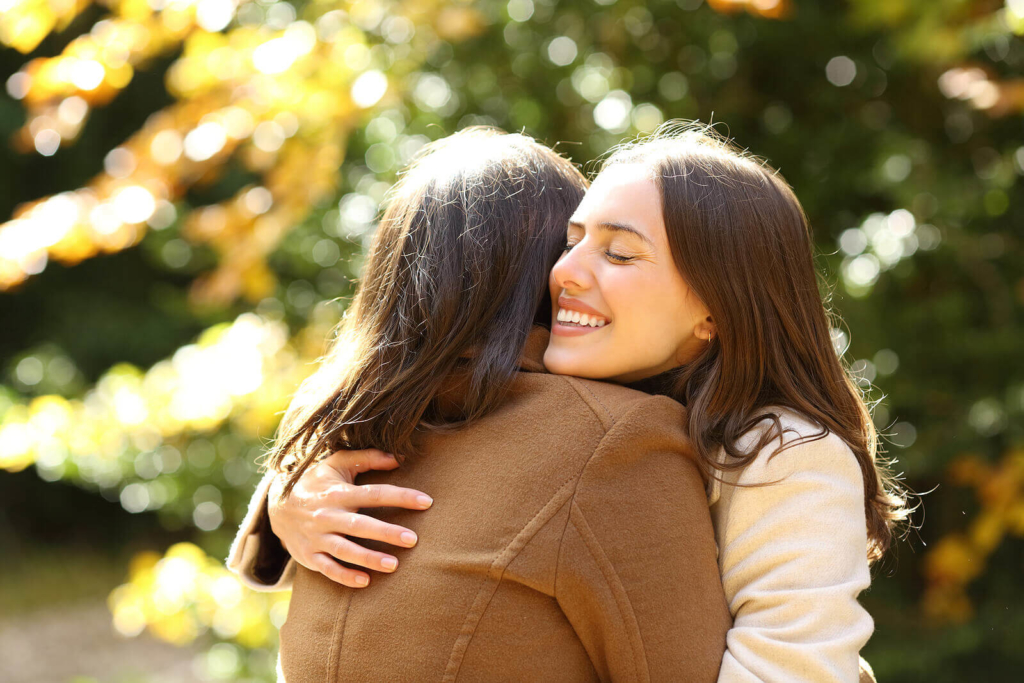 Two happy female friends with long brown hair, meeting and hugging in the park