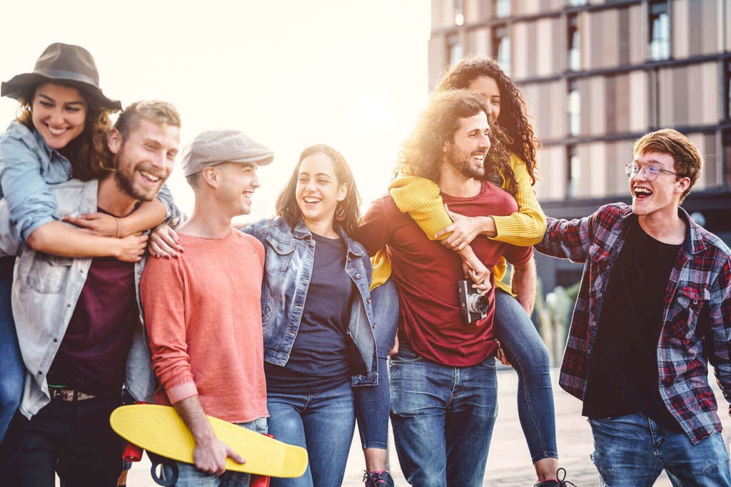 A group of smiling students in casual clothing, walking together, with two of them giving piggybacks to others