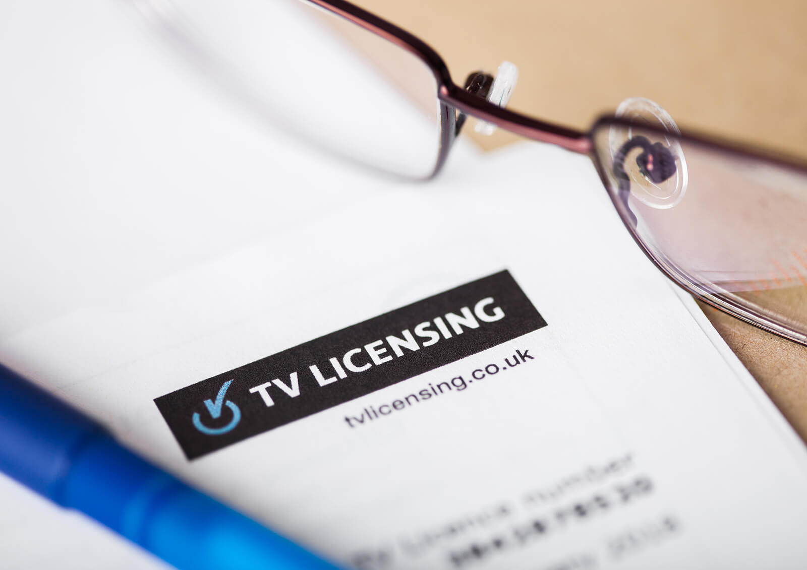 A close-up of a letter from TV Licensing about a TV licence, with spectacles and a pen in shot