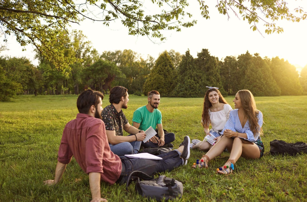 A group of five students sat in the park together, studying and smiling.