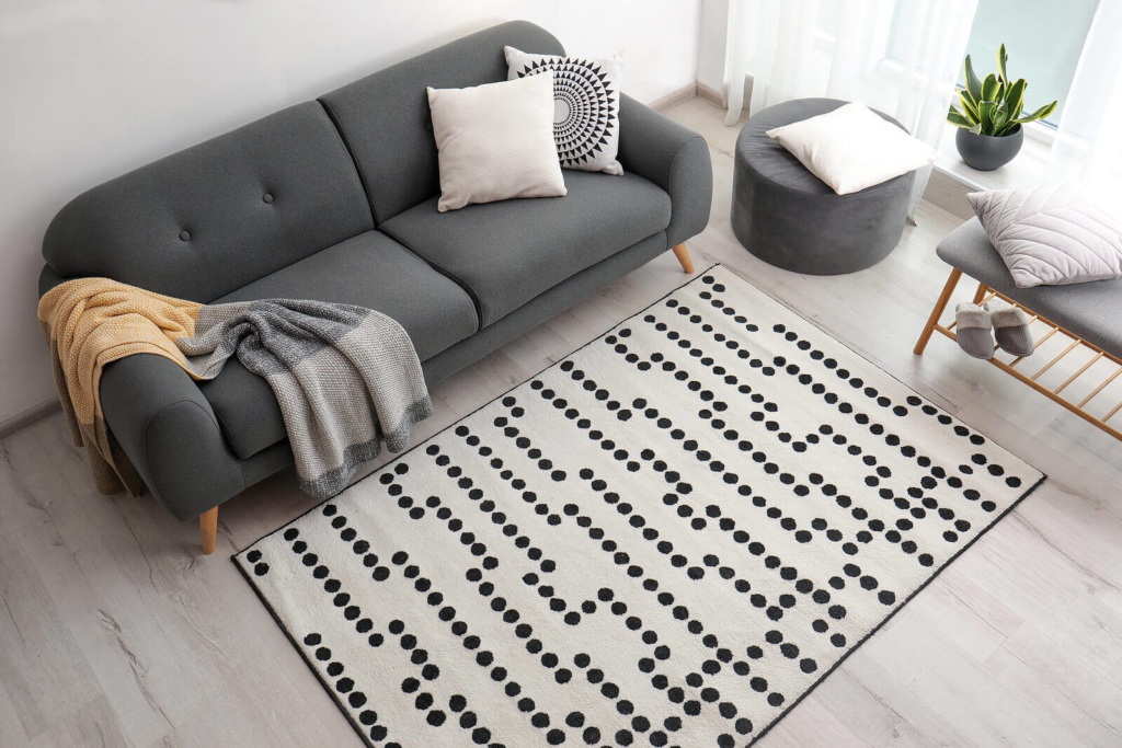 An aerial view of a living room, with a grey sofa, cream and white dotty rug, various cushions, and a throw.