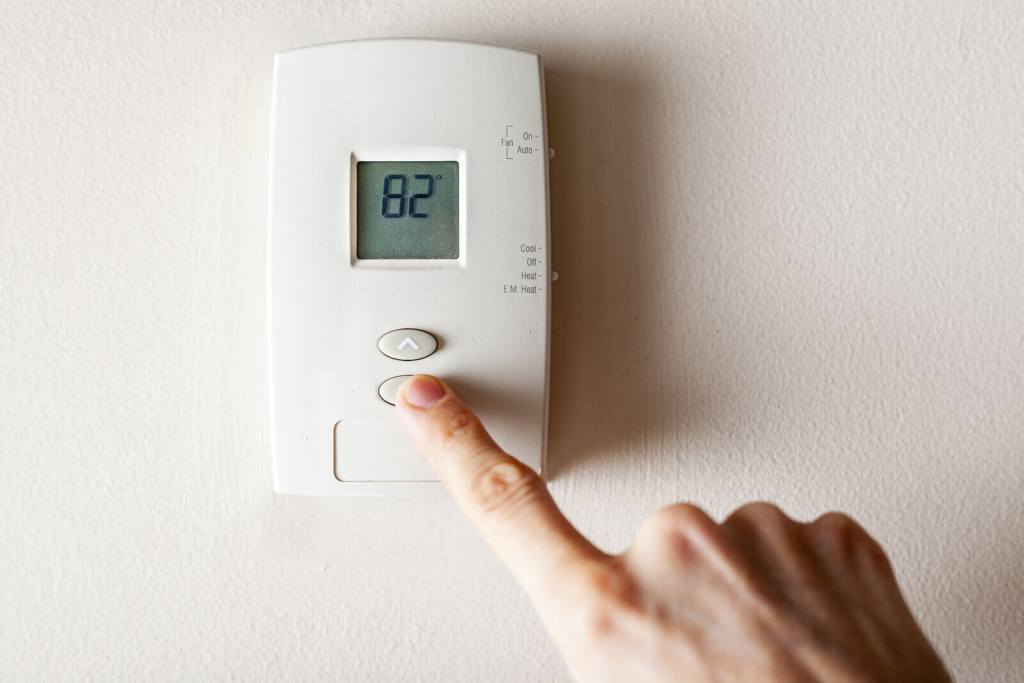 A hand using a heating thermostat on a white wall.