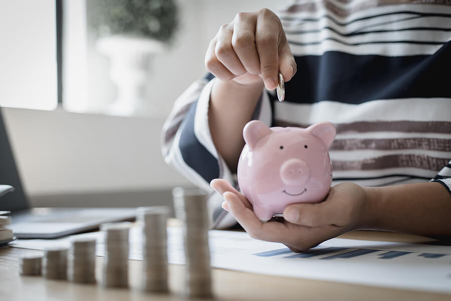 Businesswoman's hand holds money or coins into a piggy bank, Managing money or saving money for future use, Saving for investment, Saving money for business growth or long-term profitability.