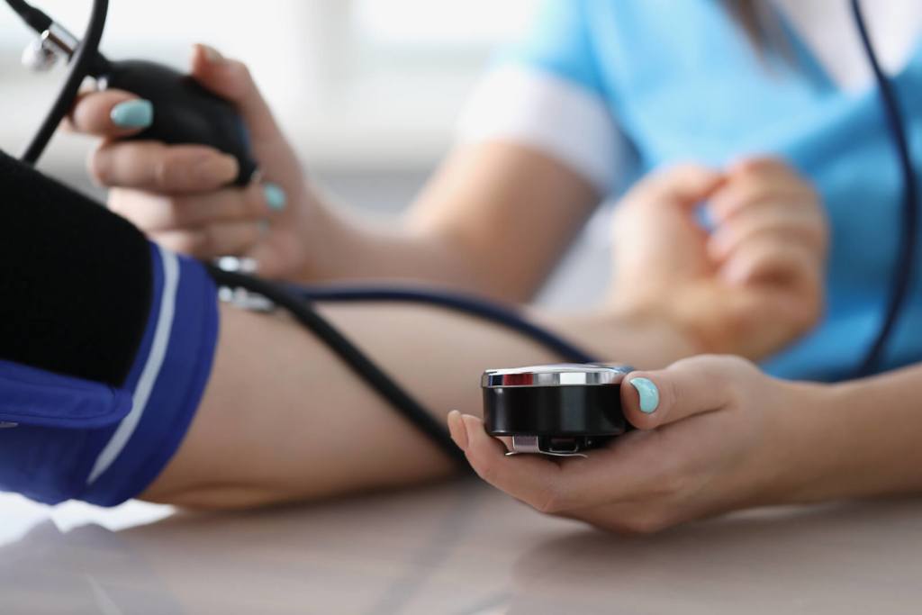 Close-up of doctor measuring patients blood pressure with tonometer tool on planned appointment.