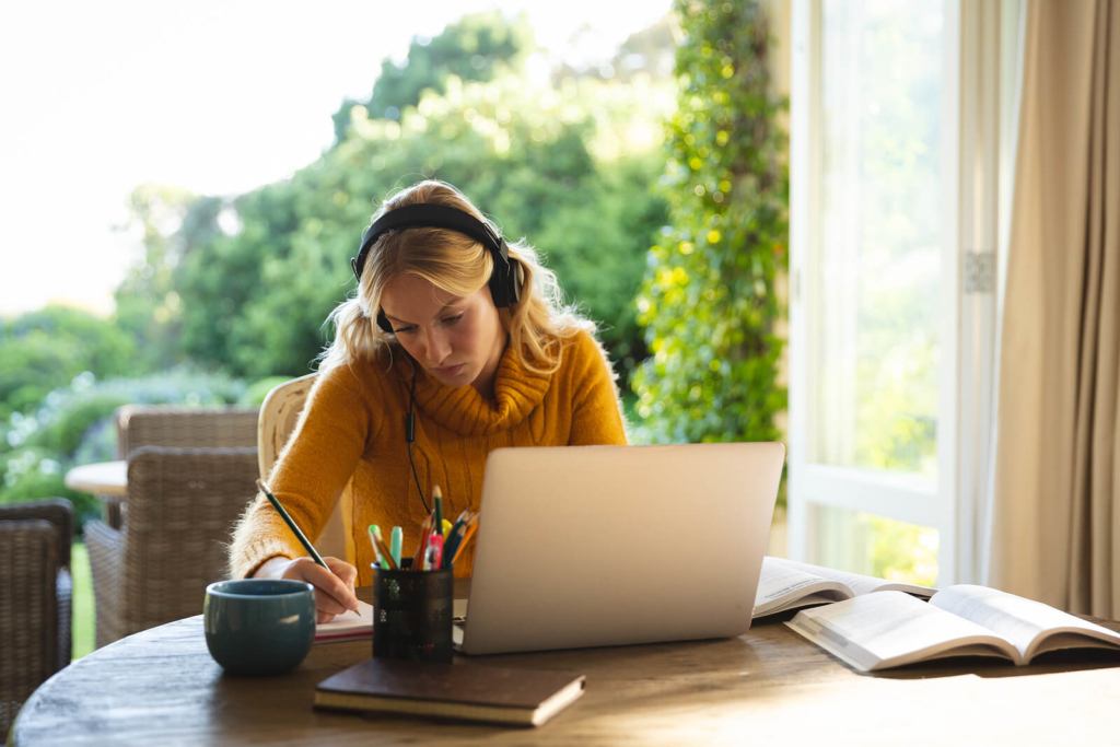 Woman working on laptop wearing headphones and a yellow jumper.