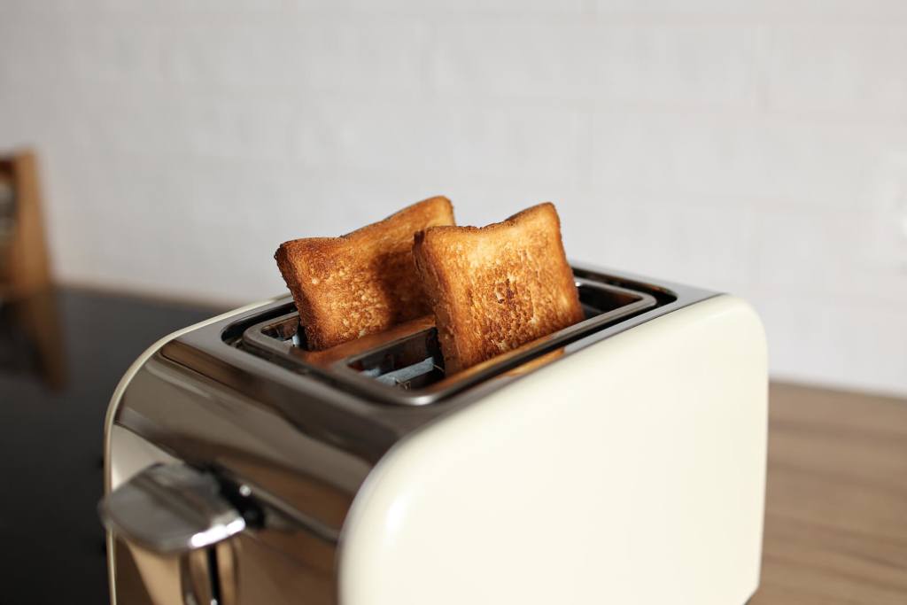 toasted grain bread in white toaster, roasted sandwich toast, concept of healthy eating, dieting, snacking at work, at school, student fast food. Modern white toaster