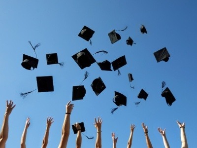 Graduation caps being thrown in the air against a blue sky