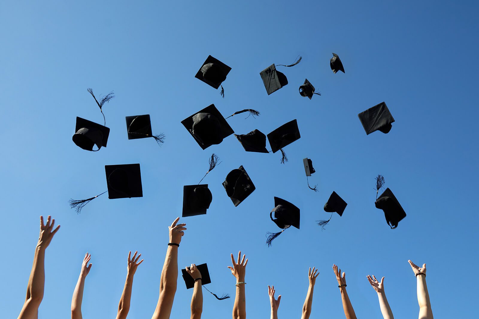 Graduation caps being thrown in the air against a blue sky