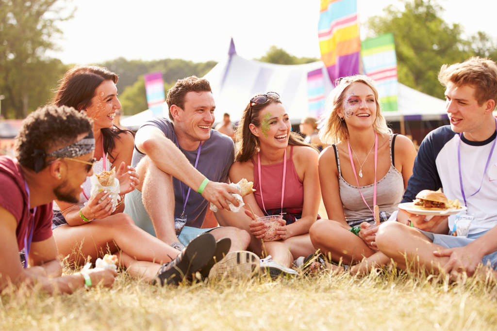 Friends sitting on grass and eating at music festival.