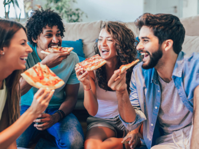 Four students eating pizza, sat in the lounge of their house share.