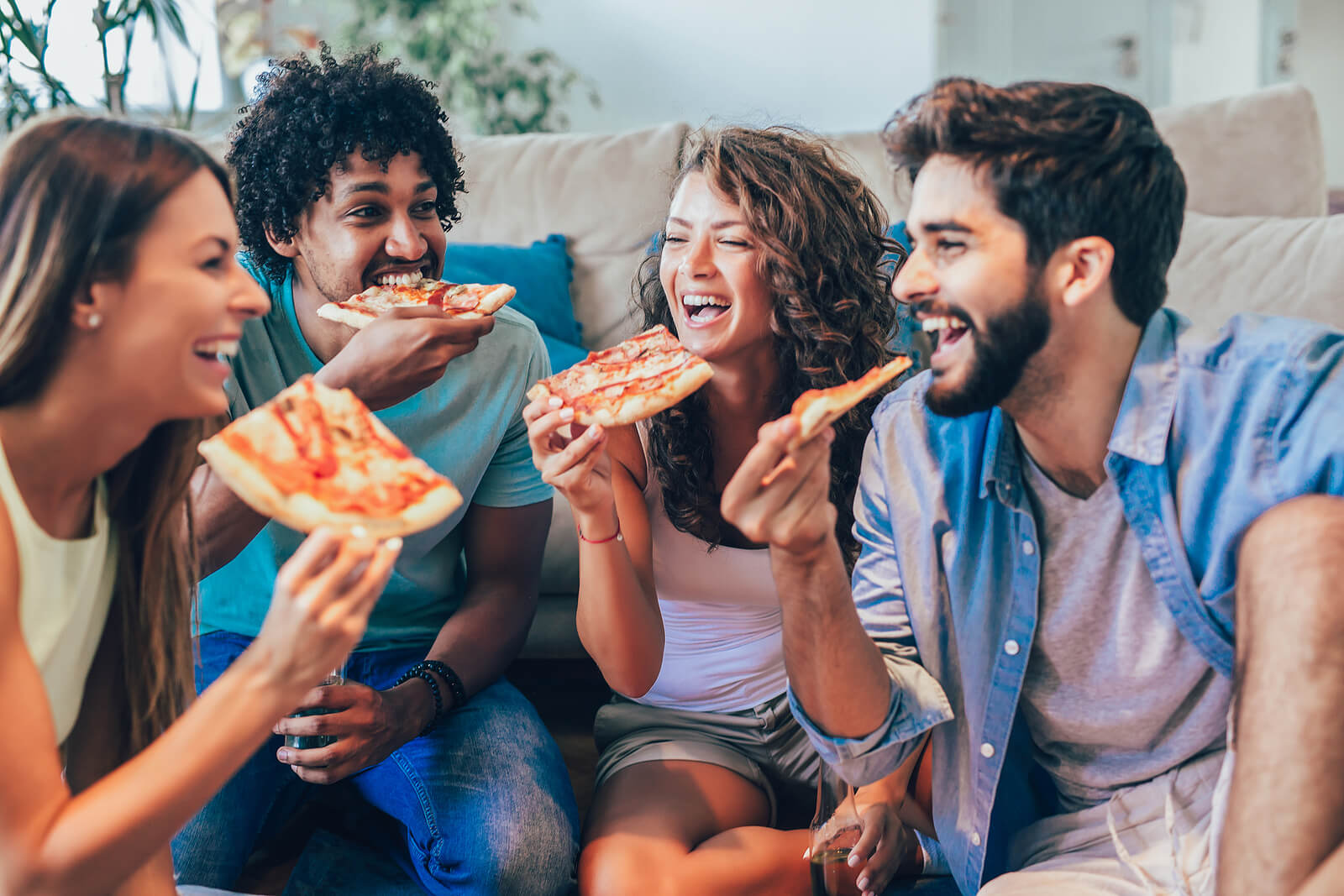 Four students eating pizza, sat in the lounge of their house share.