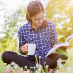 A woman reading a book, sat on grass.
