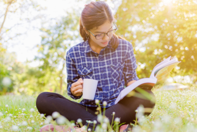 A woman reading a book, sat on grass.