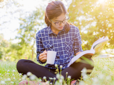 A woman reading a book, sat on grass.