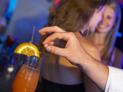 A man spiking a woman's drink in a bar or nightclub.