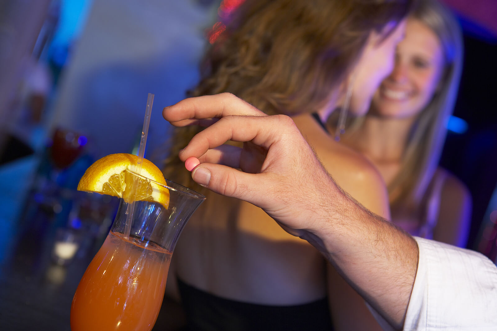 A man spiking a woman's drink in a bar or nightclub.