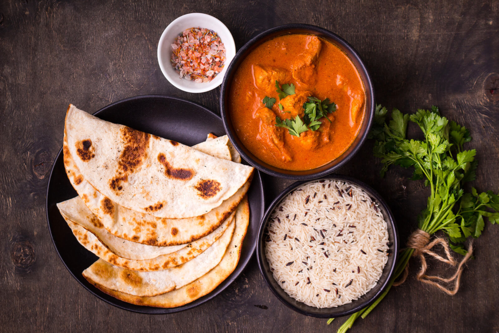 A chicken tikka masala laid out on a table with rice and breads